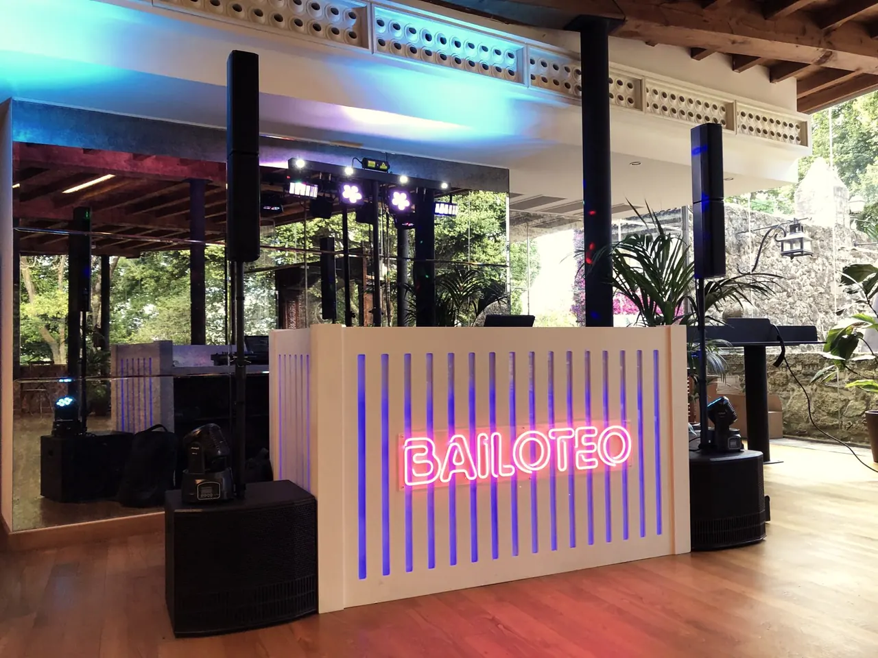 Cabina DJ blanca de lamas con neón rosa «BAILOTEO» en un salón de bodas