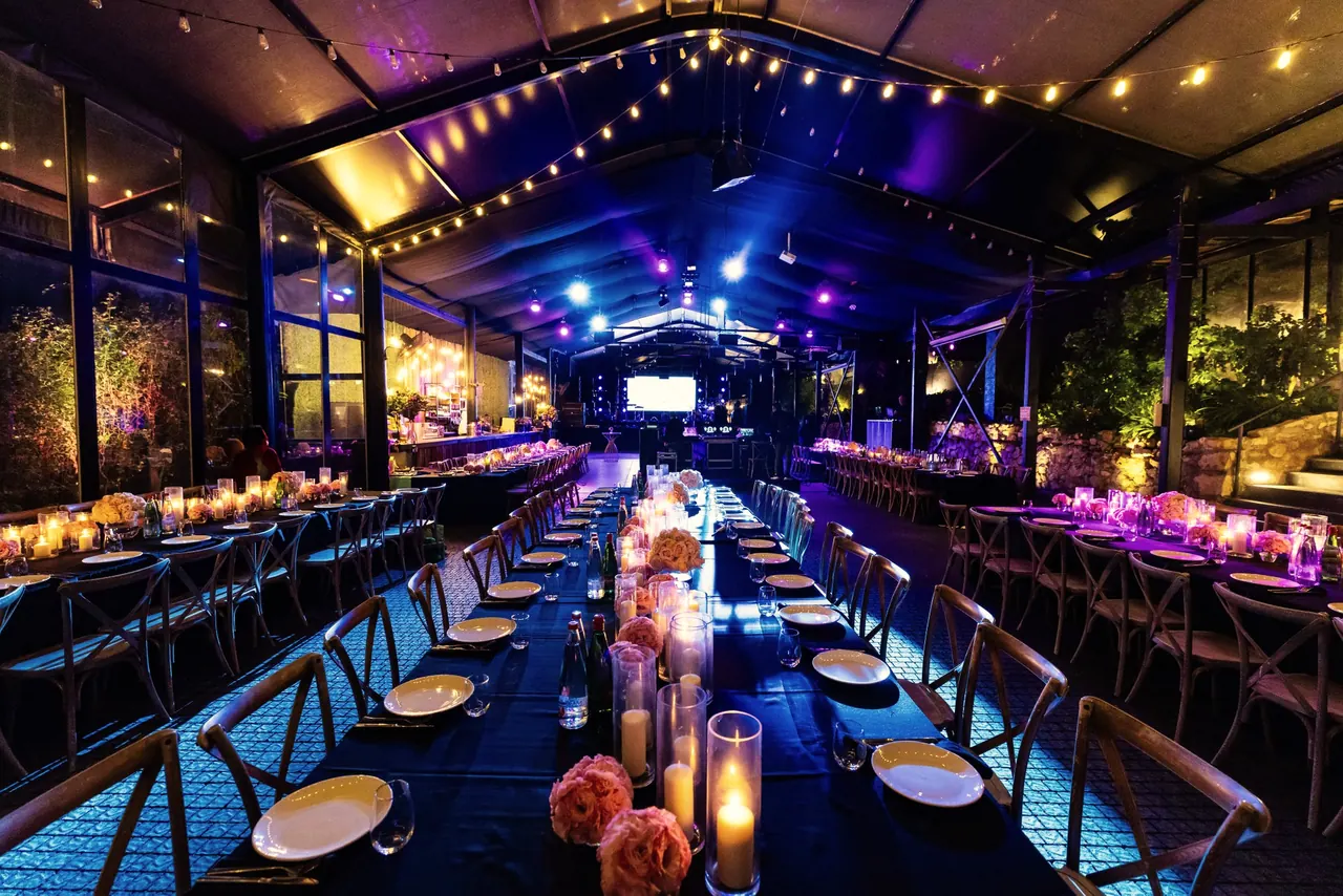 Cena de gala en una carpa iluminada con mesas largas, velas y guirnaldas de luces