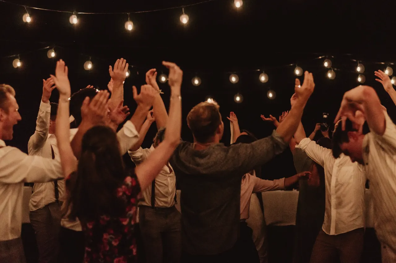 Amigos bailando con las manos arriba bajo guirnaldas de luces